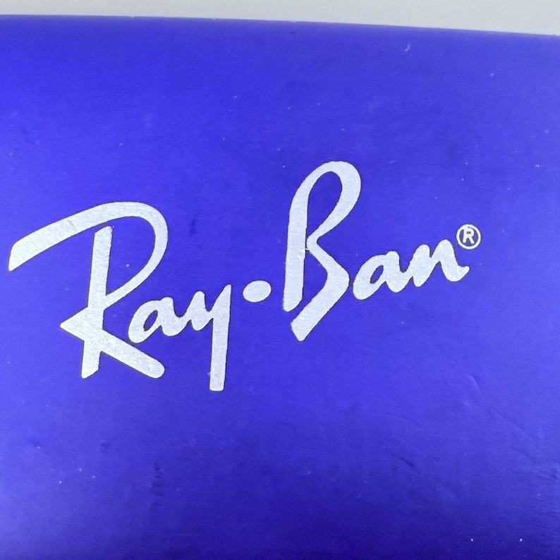 Estuche rígido azul para gafas Ray-Ban con interior rojo y acabado mate tipo concha. imagen 6
