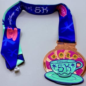 May include: A bronze-colored medal with a teal teacup design and the text "Virtual 5K" and "2020". The medal is attached to a blue ribbon with the words "Disney Virtual 5K".