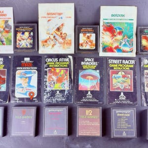 May include: A collection of six Atari video game cartridges and their corresponding instruction manuals, including titles such as Missile Command, Basketball, Berzerk, Canyon Bomber, Maze, Circus Atari, Space Invaders, Street Racer, and Indy 500.