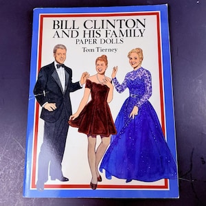 May include: A paper doll book titled Bill Clinton and His Family Paper Dolls by Tom Tierney. The cover features illustrations of three figures: a person in a black tuxedo, a person in a short dark red dress, and a person in a long blue gown.