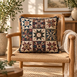 May include: A square throw pillow featuring a patchwork quilt design with a repeating star pattern. The fabric displays a color palette of deep red, navy blue, cream, and forest green, arranged in a grid of nine distinct geometric blocks.