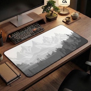 Könnte beinhalten: Rechteckige Schreibtisch-Mausunterlage mit einem Berg- und Waldlandschaftsdesign in Grau- und Weißtönen. Das Pad liegt auf einem Holzschreibtisch mit Tastatur, Monitor und Bonsai-Baum.