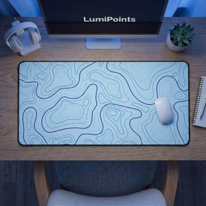 May include: A rectangular desk mat with a light blue topographic map design. The map features dark blue contour lines and dotted lines. A white computer mouse rests on the mat. The text "LumiPoints" is visible on the computer monitor.