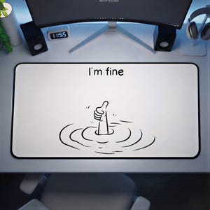 May include: White rectangular desk mat with a black border. The mat features the phrase "I'm fine" above a cartoon illustration of a hand giving a thumbs up while submerged in water. The design is in black.