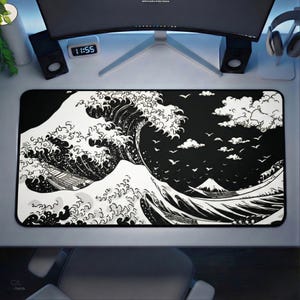 Puede incluir: Alfombrilla de escritorio rectangular en blanco y negro con una representación estilizada de una gran ola oceánica, con un barco y una montaña en el fondo. El diseño recuerda al arte tradicional japonés. La alfombrilla está colocada sobre un escritorio blanco.