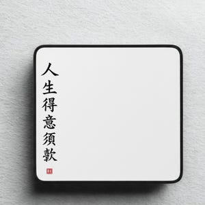 Peut inclure: Un tapis de souris rectangulaire blanc avec une bordure noire. Le tapis de souris présente une calligraphie chinoise noire sur le côté gauche. La calligraphie est accompagnée d'un petit tampon rouge. Le tapis est sur une surface blanche texturée.