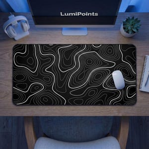May include: A black and white topographic design mouse mat with a white computer mouse. The mouse mat has a pattern of white lines on a black background. The text "LumiPoints" is visible on the computer monitor.