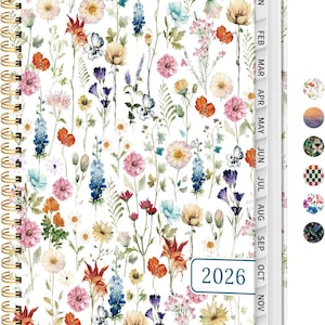 May include: A floral-patterned 2026 planner with a gold spiral binding. The cover features a white background with watercolor flowers in shades of pink, orange, blue, and yellow. Monthly tabs are visible on the side.