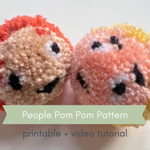 以下が含まれることがあります： 人型のハンドメイドポンポンが2つ。オレンジ色の髪と黄色の髪があります。どちらも黒い目と笑顔です。「People Pom Pom Pattern」と「printable + video tutorial」の文字が緑色のバナーにあります。