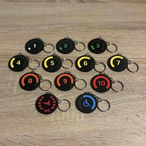 May include: A collection of twelve circular black keychains, each featuring a silver metal ring. Eleven keychains display numbers one through ten in various colors, while one features a red arrow icon and another a blue wheelchair symbol.
