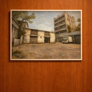 May include: A framed painting depicting an urban scene with a warehouse and a multi-story building under a cloudy sky. The warehouse has a large door with the letter "A" visible. A white truck is parked nearby.