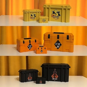 May include: A collection of yellow, orange, and black storage boxes of varying sizes. Each box features unique graphic designs and text. The boxes are arranged on white shelves against a yellow curtain backdrop.