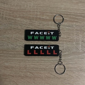May include: Two rectangular black keychains featuring the white text FACEIT with an orange arrow. One keychain displays five green W letters, while the other keychain displays five red L letters. Both items include a silver metal ring and chain.