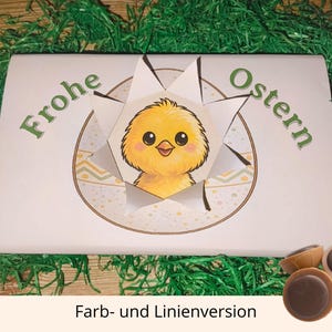 May include: A white Easter-themed gift box with the words "Frohe Ostern" in green. The box features a yellow chick illustration and is surrounded by green decorative grass. Several chocolate candies are visible.