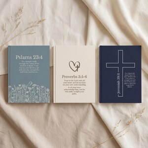 Op de afbeelding: Drie hardcover journals met religieuze citaten. De eerste is blauw met "Psalms 23:4", de tweede is crème met "Proverbs 3:5-6", en de derde is marineblauw met "Jeremiah 29:11". Elk journal heeft een uniek ontwerp.