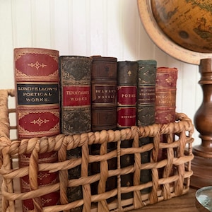May include: A collection of six antique hardcover books with leather spines in a woven wicker basket. The books feature gold-embossed lettering and decorative patterns, with titles including Longfellow's Poetical Works, Tennyson's Works, and Bulwer's Novels.