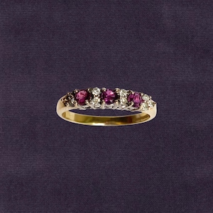 Peut inclure: Une bague en or ornée de trois pierres précieuses magenta taille ronde alternant avec des pierres blanches transparentes plus petites. La monture est en métal et présente un alignement horizontal de pierres sur le dessus de l'anneau.