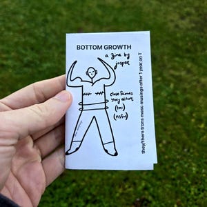 Peut inclure: Un petit fanzine blanc intitulé "BOTTOM GROWTH" par Jasper, tenu dans une main. La couverture présente une illustration en noir et blanc d'une personne les bras levés. Le texte comprend "close friends story edition (tmi) (nsfw)" et "they/them trans masc musings after 1 year on T."