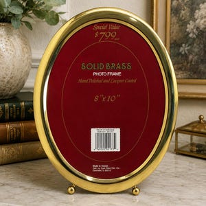 May include: An oval solid brass photo frame with a polished finish and lacquer coating. The frame features a deep red insert with text reading Special Value $799, SOLID BRASS PHOTO FRAME, Hand Polished and Lacquer Coated, and 8"x 10".