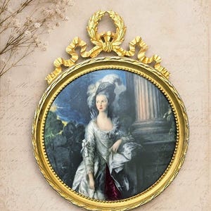 May include: An oval portrait painting encased in an ornate gold frame with a laurel wreath and ribbon crest at the top. The artwork depicts a person in a white gown and feathered headpiece standing beside a stone pillar in a dark landscape.
