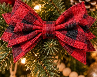 May include: A decorative bow featuring a red and black buffalo plaid pattern with a textured fabric finish. The text Buffalo Plaid Christmas Bows Set of 5 or 10 is displayed above the bow, which is positioned against a green pine branch.