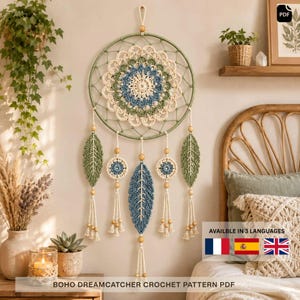 Op de afbeelding: Een ronde wandhanger met een centraal gehaakt mandala in crème, saliegroen en stoffig blauw. Het ontwerp bevat vijf hangende elementen: twee bladvormige gehaakte stukken in groen, twee kleine ronde gehaakte motieven en een groot centraal blauw blad.