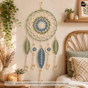 May include: A circular wall hanging featuring a multi-layered crochet mandala in shades of cream, sage green, and dusty blue. The piece includes dangling crochet leaves and circular motifs accented with wooden beads, suspended from a green hoop.