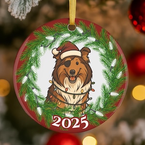 May include: A round Christmas ornament with a red border and a festive design. The ornament features a cartoon dog wearing a Santa hat and a string of lights, surrounded by a green wreath. The year "2025" is printed at the bottom.