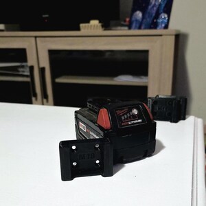 May include: Black and red Milwaukee M18 REDLITHIUM battery pack with a black M18 battery holder. The battery pack has a red top and the words "Milwaukee" and "REDLITHIUM" printed on it. The battery holder has the letters "M18" printed on it.