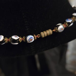 May include: A necklace with black and white glass beads, each with a floral pattern. The beads are strung together with red thread and gold-coloured metal. It has a brass clasp.