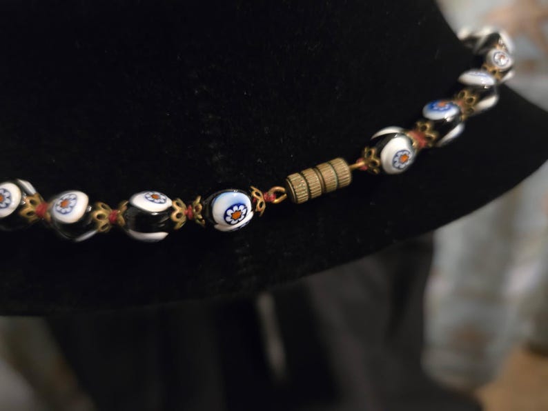 May include: A necklace with black and white glass beads, each with a floral pattern. The beads are strung together with red thread and gold-coloured metal. It has a brass clasp.