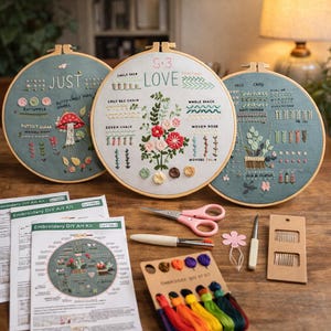 Può includere: Tre opere d'arte con ricamo su telaio con motivi floreali e a punto. I telai sono esposti con materiali per ricamo, tra cui forbici, aghi e filo colorato. Il testo sui telai include "JUST" e "LOVE".