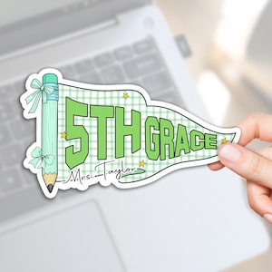 May include: A pennant-shaped sticker featuring a light green pencil with two bows on the left side. The background has a light green gingham pattern with small yellow stars. The text reads 5TH GRADE and Mrs. Taylor in black script.