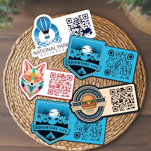 May include: Five rectangular stickers with QR codes and graphic designs. One features a blue hot air balloon labeled National Park Holidays, two show palm trees and the text Adventure Life, one displays a geometric fox, and one shows a burger.