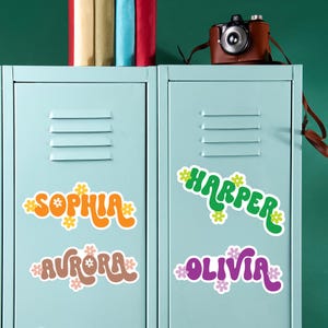 May include: Light blue lockers with colorful name stickers. The stickers feature the names Sophia, Aurora, Harper, and Olivia in various colors and floral designs. A vintage camera sits on top of the lockers.