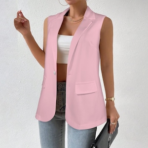 Op de afbeelding: Een mouwloze, lichtroze blazer met een revers en een sluiting met één knoop. De blazer heeft twee voorzakken en een getailleerde pasvorm. Het model draagt de blazer met een witte top en een blauwe jeans.