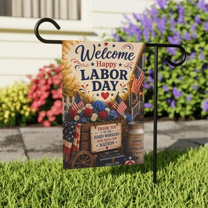 Könnte beinhalten: Eine rechteckige Gartenflagge an einem schwarzen Metallständer. Die Flagge zeigt den Text Welcome Happy LABOR DAY und THANK YOU TO THE HARD WORKERS WHO BUILD OUR NATION. Sie zeigt eine Holzkiste mit roten, weißen und blauen Blumen.