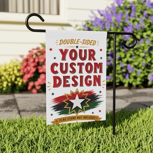 May include: A white, double-sided garden flag with the text "YOUR CUSTOM DESIGN" in red. The flag features a starburst design with red, black, and green accents. The flag is displayed on a black metal stand in a garden setting.