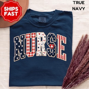 Könnte beinhalten: Ein marineblaues T-Shirt mit dem Wort "NURSE" in einem Design im College-Stil. Die Buchstaben weisen Muster wie Sterne, Vichy, Tupfen und Streifen auf, mit medizinischen Symbolen wie Herzen und Stethoskopen. Das T-Shirt hat einen Rundhalsausschnitt.