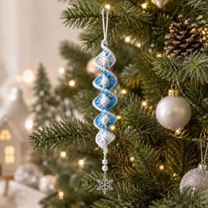 May include: A spiral-shaped crochet ornament featuring alternating white and light blue yarn sections. The ornament hangs from a white loop and is finished at the bottom with two small white beads and a silver-toned metal snowflake charm.