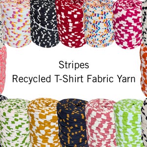 Può includere: Una collezione di filato di tessuto di maglietta riciclato a righe colorate in varie tonalità, tra cui rosa, arancione, nero, bianco e blu. L'immagine mostra diversi rocchetti di filato, con il testo "Stripes Recycled T-Shirt Fabric Yarn".