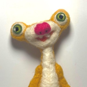 May include: A handmade felt sculpture of a cartoon sloth character. The sloth has a yellow body, a white face and neck, a bright pink nose, and large green eyes. The sloth is smiling.