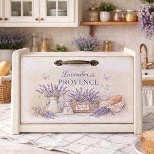 Może przedstawiać: Biała drewniana chlebownica z dekoracyjnym frontem z motywem lawendy i napisem "Lavender de PROVENCE". Chlebownica ma metalowy uchwyt i jest prezentowana w otoczeniu kuchni.