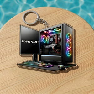May include: A computer-themed keychain featuring a desktop computer, monitor, keyboard, and mouse. The computer case has colorful LED lights. The monitor displays "YOUR NAME". The keychain is attached to a silver ring.
