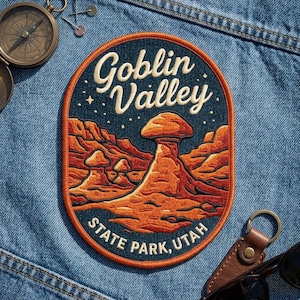 May include: An oval embroidered patch featuring a dark blue night sky with stars above a landscape of orange and red rock formations. The text reads Goblin Valley in cream script and STATE PARK, UTAH in cream block letters with an orange border.