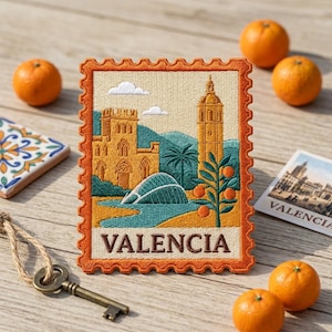 May include: A rectangular embroidered patch shaped like a postage stamp featuring a landscape of Valencia, Spain. The design includes a yellow stone building, a tall tower, a blue structure, and an orange tree. The word VALENCIA is stitched in brown.