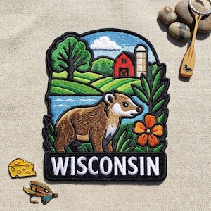 May include: An embroidered patch featuring a brown badger in a landscape with a red barn, green hills, a blue river, and a large orange flower. The word WISCONSIN is stitched in white capital letters at the bottom on a black background.