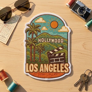May include: An embroidered patch featuring a landscape scene with palm trees, green hills, a bright orange sun, and white clouds. The text HOLLYWOOD is centered above a black film clapperboard, with the text LOS ANGELES at the bottom in bold letters.
