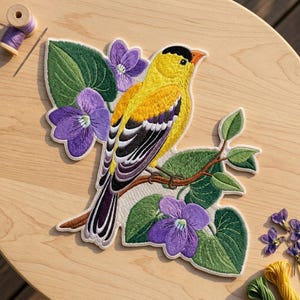 May include: An embroidered patch featuring a yellow goldfinch with black and white wing markings perched on a brown branch. The bird is surrounded by vibrant purple violet flowers and large green leaves, all rendered in detailed thread work.
