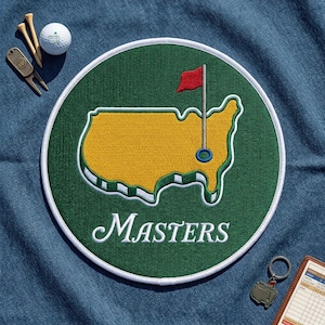 May include: A circular embroidered patch featuring a yellow map of the United States on a green background with a red flag and the word Masters in white script. Accessories include two wooden golf tees, a white golf ball, and a metal keychain.